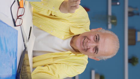 Vertical-video-of-Home-office-worker-old-man-making-cute-gesture-at-camera.